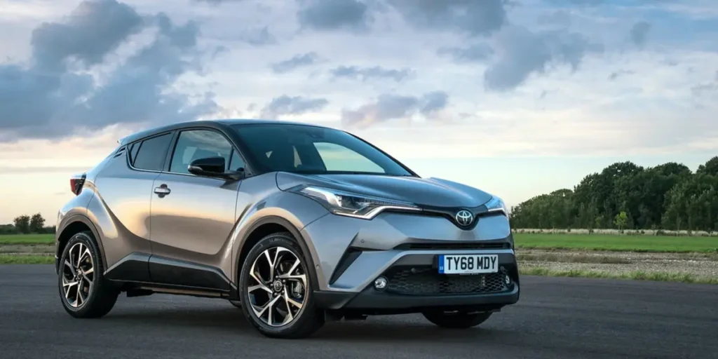 Silver Toyota C-HR parked on a road with a field and trees in the background.