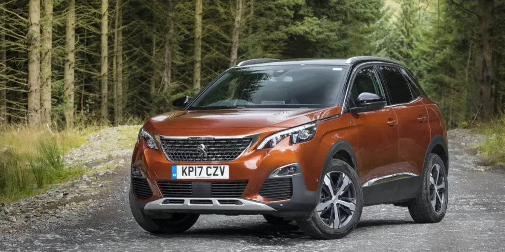 A brown Peugeot 3008 SUV parked on a dirt road in a forest. The car has alloy wheels and a rugged design. The license plate on the car is KP17 CZV.