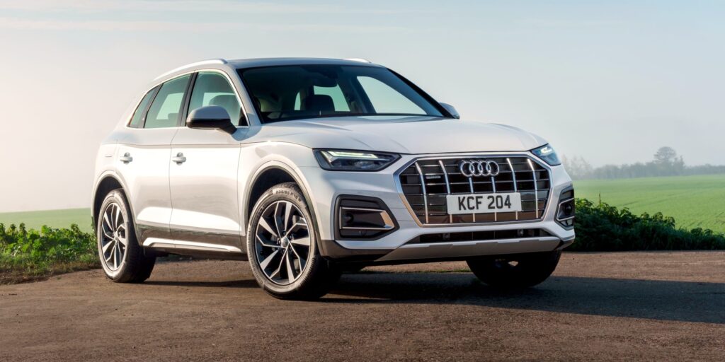 White Audi Q5 SUV parked on a dirt road with a field in the background.