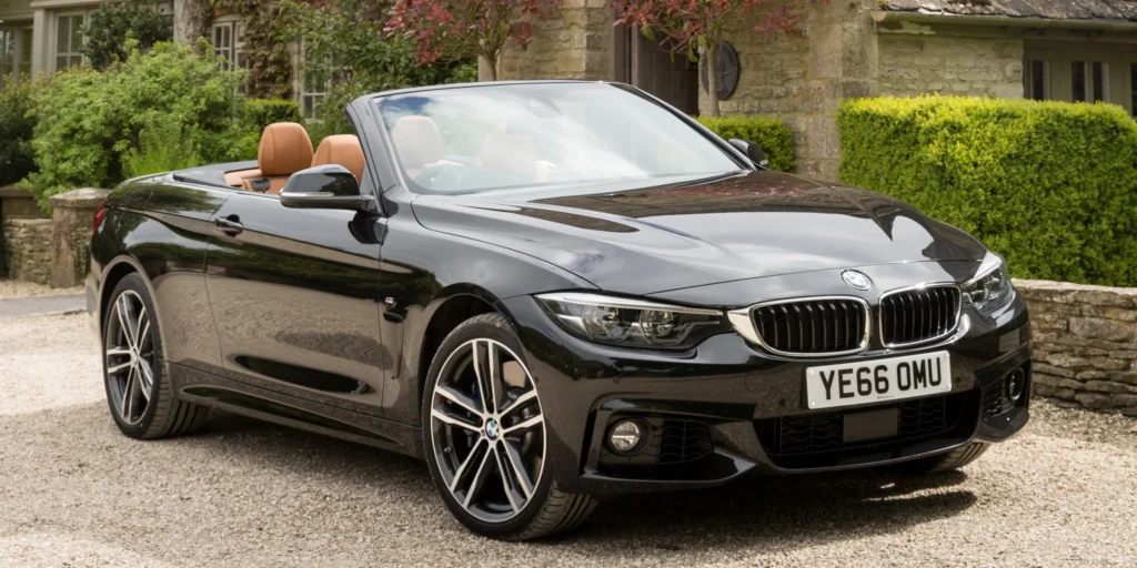 Black BMW 4 Series Convertible parked in front of a house with a green hedge.