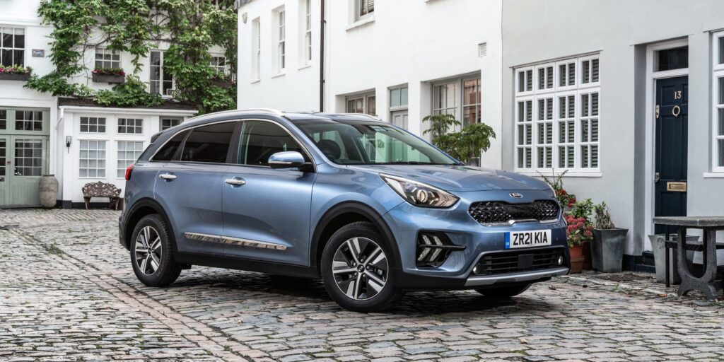 Blue Kia Niro parked on a cobblestone street in front of a historic building.