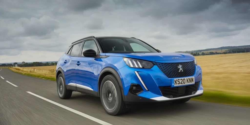 Blue Peugeot e-2008 SUV driving on a road with a field in the background.