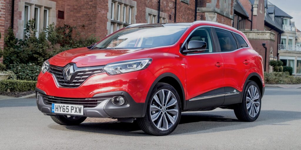 A red Renault Kadjar SUV parked on a street in front of a brick building. The car has alloy wheels and a modern design. The license plate on the car is HY65 PXW.