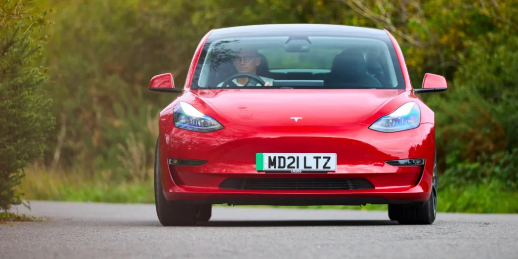 Red Tesla Model 3 driving on a winding road with trees on either side.