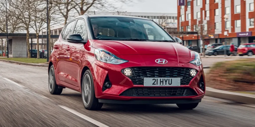 Red Hyundai i10 car driving on a street.