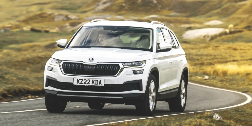 White Škoda Karoq driving on a winding road in a mountainous landscape.